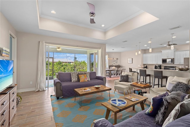 living room featuring crown molding, light hardwood / wood-style flooring, a raised ceiling, and ceiling fan