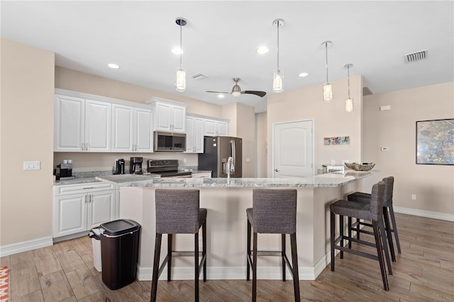 kitchen with white cabinets, a kitchen bar, hanging light fixtures, light hardwood / wood-style floors, and stainless steel appliances