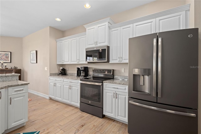 kitchen with light stone countertops, white cabinetry, appliances with stainless steel finishes, and light wood-type flooring