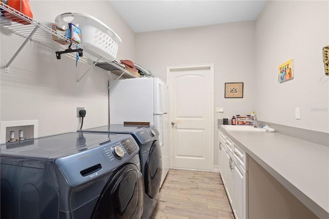 clothes washing area featuring cabinets, sink, washer and dryer, and light wood-type flooring