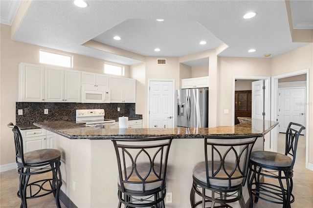 kitchen featuring white appliances, a breakfast bar area, a center island, decorative backsplash, and white cabinetry