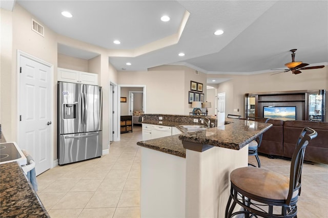 kitchen with stainless steel refrigerator with ice dispenser, a kitchen bar, white cabinetry, ceiling fan, and sink