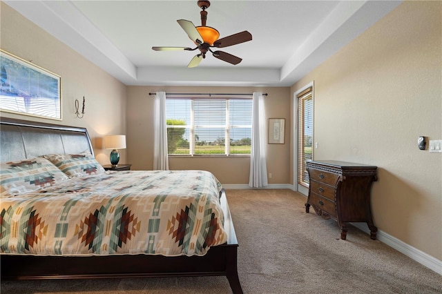 carpeted bedroom with a raised ceiling and ceiling fan