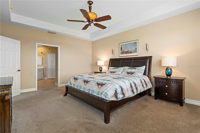 carpeted bedroom with a raised ceiling, ceiling fan, and ensuite bath