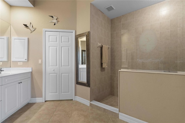 bathroom with tile patterned flooring, tiled shower, and vanity