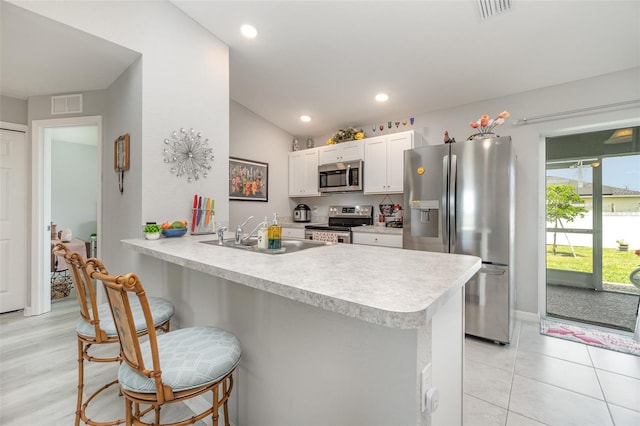 kitchen featuring stainless steel appliances, sink, white cabinets, a kitchen bar, and kitchen peninsula