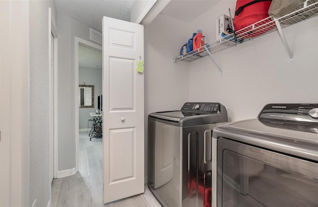 laundry room featuring a textured ceiling, light wood-type flooring, and washing machine and clothes dryer