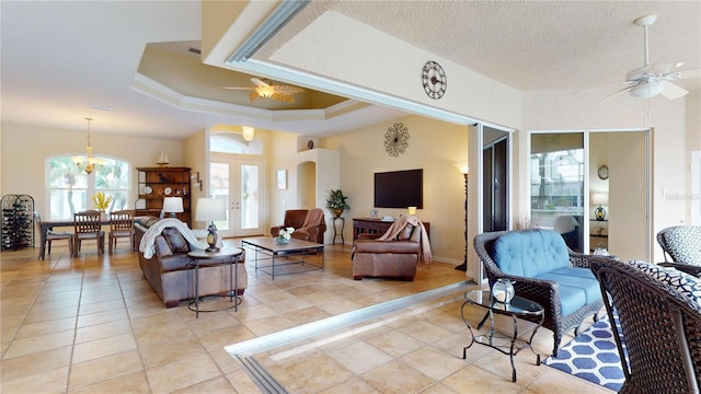 tiled living room with a textured ceiling, ceiling fan with notable chandelier, french doors, and a tray ceiling