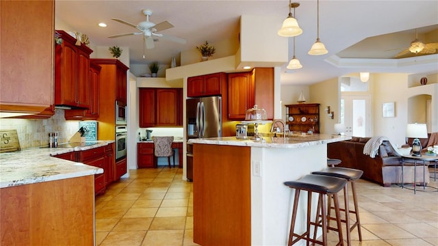 kitchen featuring pendant lighting, stainless steel appliances, decorative backsplash, ceiling fan, and a tray ceiling