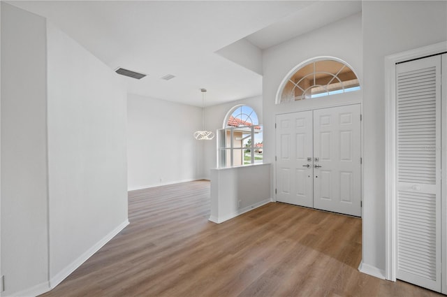 foyer entrance with a towering ceiling, an inviting chandelier, and light wood-type flooring