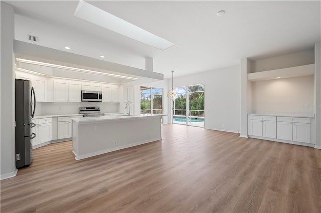 kitchen featuring stainless steel appliances, an island with sink, sink, white cabinetry, and decorative light fixtures