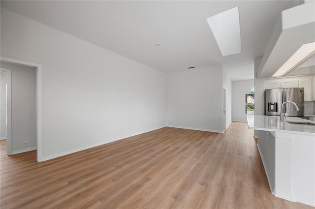 unfurnished living room with light wood-type flooring, a skylight, and sink