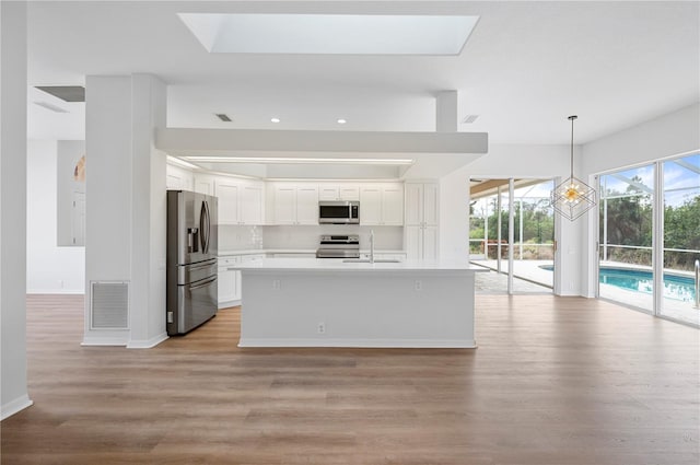 kitchen featuring stainless steel appliances, white cabinets, light hardwood / wood-style flooring, decorative light fixtures, and sink