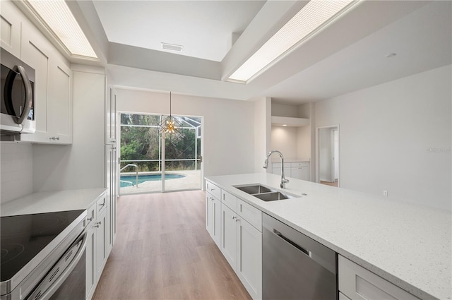 kitchen with white cabinets, stainless steel appliances, light wood-type flooring, hanging light fixtures, and sink