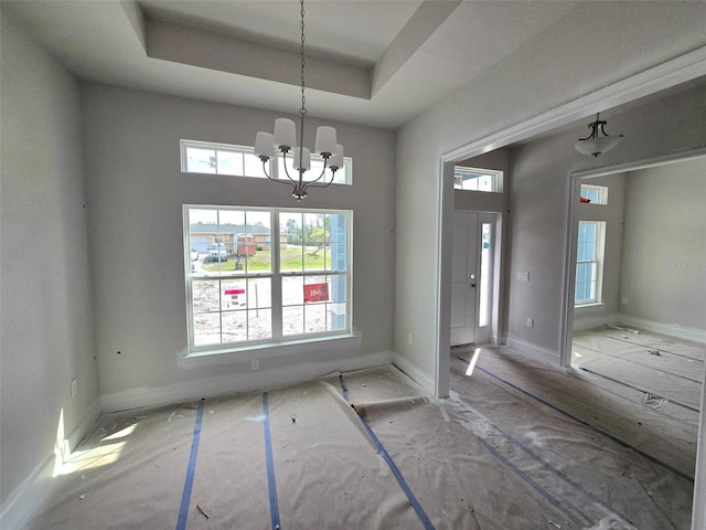 unfurnished dining area with a chandelier, a raised ceiling, and baseboards