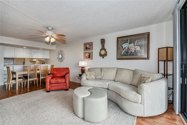 living room featuring ceiling fan, a textured ceiling, and light wood-type flooring