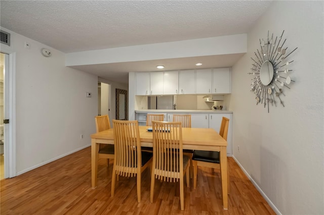 dining area with a textured ceiling and light hardwood / wood-style floors