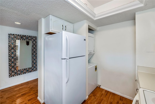 kitchen featuring white fridge, white cabinetry, stacked washer and clothes dryer, hardwood / wood-style flooring, and range