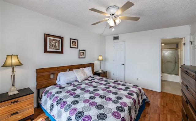 bedroom with ceiling fan, connected bathroom, hardwood / wood-style flooring, and a textured ceiling