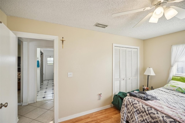 bedroom featuring light tile patterned floors, a closet, ceiling fan, and a textured ceiling