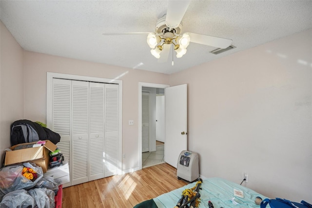 bedroom with a textured ceiling, wood-type flooring, ceiling fan, and a closet