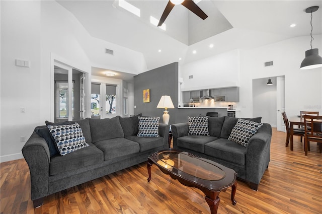 living room with ceiling fan, wood-type flooring, and a towering ceiling