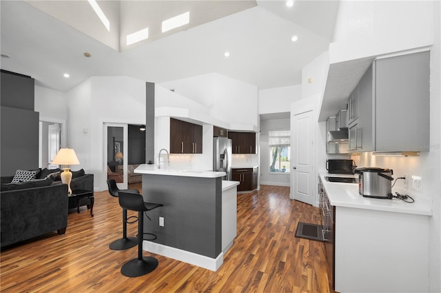 kitchen with kitchen peninsula, stainless steel fridge, a breakfast bar area, dark hardwood / wood-style floors, and high vaulted ceiling