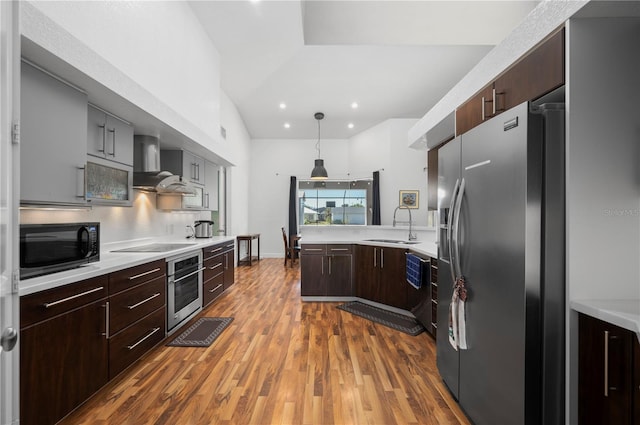 kitchen with hardwood / wood-style floors, appliances with stainless steel finishes, wall chimney exhaust hood, decorative light fixtures, and sink