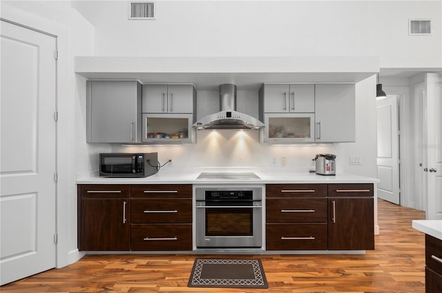 kitchen with decorative backsplash, black appliances, wall chimney exhaust hood, and light wood-type flooring