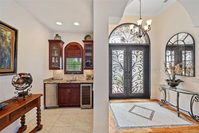 entrance foyer with light tile patterned floors, wine cooler, wet bar, french doors, and a chandelier