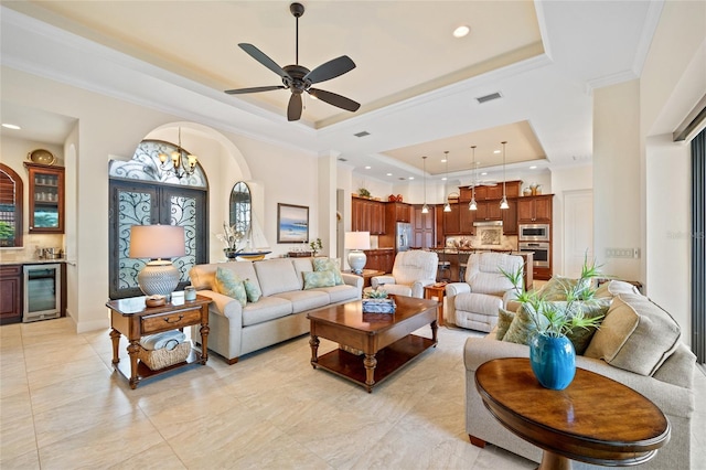 living room with wine cooler, indoor bar, ornamental molding, a tray ceiling, and ceiling fan with notable chandelier