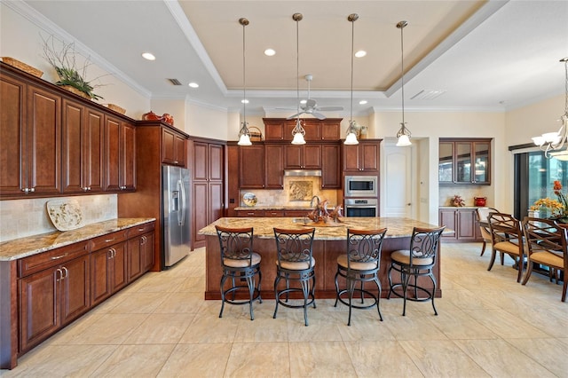 kitchen with pendant lighting, appliances with stainless steel finishes, light stone counters, decorative backsplash, and a large island with sink