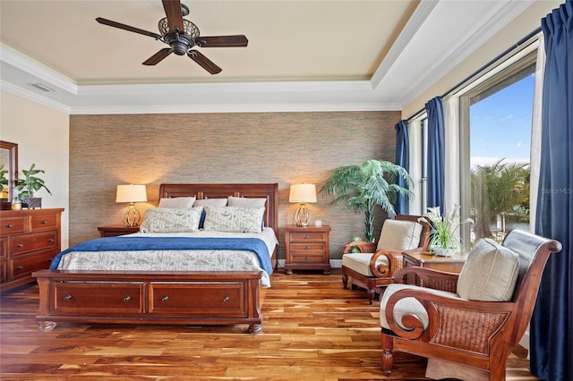 bedroom with ceiling fan, ornamental molding, a raised ceiling, and light hardwood / wood-style flooring