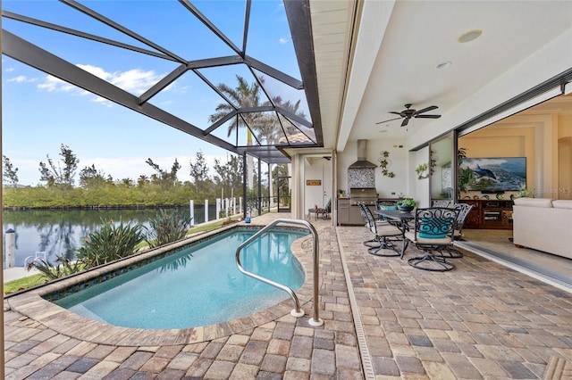 view of swimming pool with an outdoor kitchen, a water view, a patio, ceiling fan, and a lanai