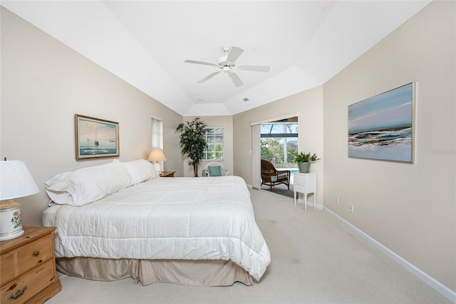 bedroom featuring ceiling fan, light colored carpet, vaulted ceiling, and a tray ceiling