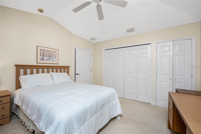 bedroom with ceiling fan, light colored carpet, lofted ceiling, and multiple closets