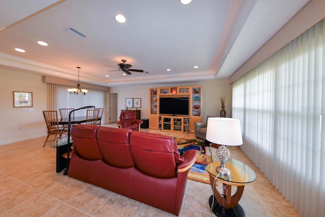 living room with light tile patterned flooring, ornamental molding, a tray ceiling, and ceiling fan with notable chandelier