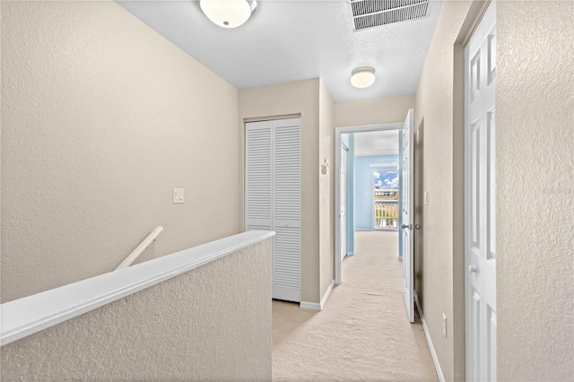 hallway with a textured ceiling and light carpet