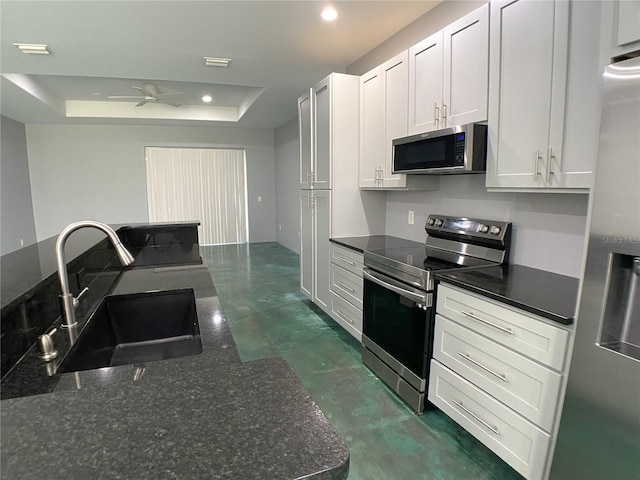 kitchen with sink, white cabinetry, appliances with stainless steel finishes, a tray ceiling, and dark stone counters