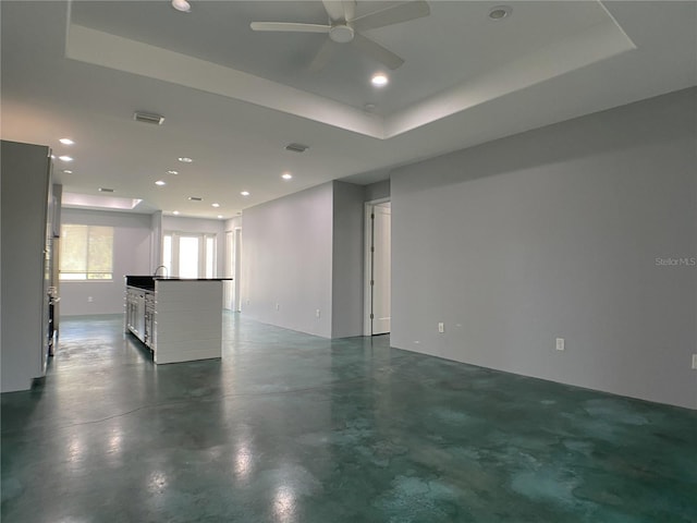 unfurnished living room with a tray ceiling, concrete flooring, and ceiling fan