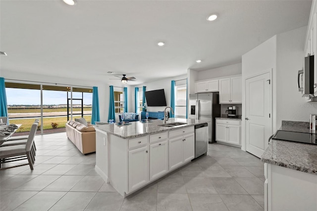 kitchen with stainless steel appliances, a kitchen island with sink, light stone countertops, white cabinets, and sink