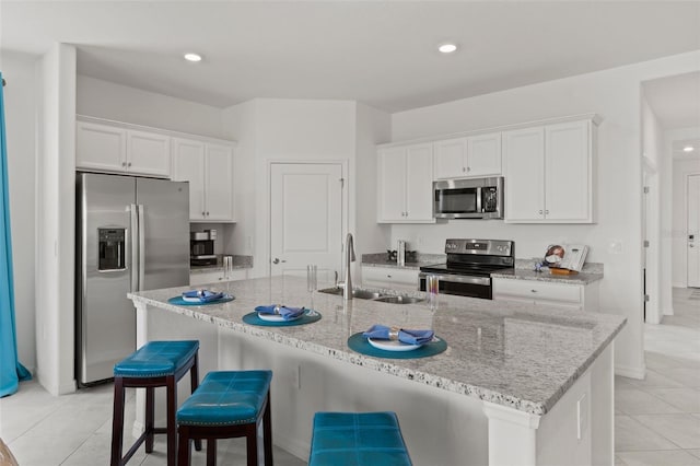 kitchen with white cabinets, appliances with stainless steel finishes, a kitchen island with sink, and light tile patterned flooring