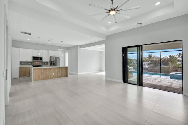 kitchen with appliances with stainless steel finishes, white cabinetry, an island with sink, decorative backsplash, and ceiling fan