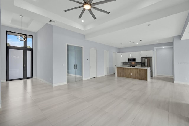 unfurnished living room featuring ceiling fan with notable chandelier and a raised ceiling