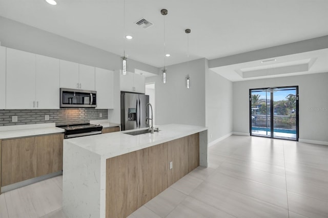 kitchen with white cabinetry, stainless steel appliances, sink, hanging light fixtures, and a kitchen island with sink