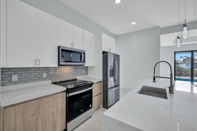 kitchen with white cabinetry, appliances with stainless steel finishes, decorative light fixtures, light stone countertops, and sink