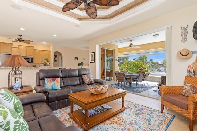 living room featuring ceiling fan, light tile patterned floors, ornamental molding, and a raised ceiling