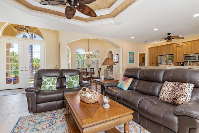 tiled living room featuring a raised ceiling, french doors, ceiling fan with notable chandelier, and ornamental molding