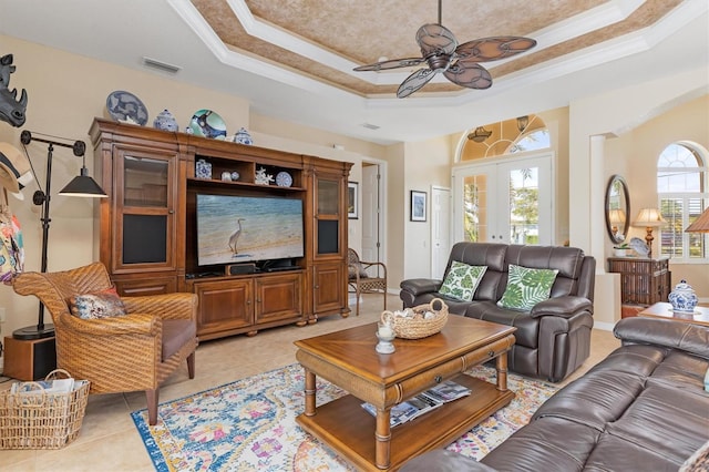 tiled living room with ceiling fan, ornamental molding, french doors, and a tray ceiling