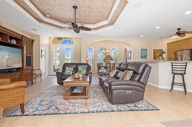 living room featuring ceiling fan with notable chandelier, a tray ceiling, ornamental molding, and french doors